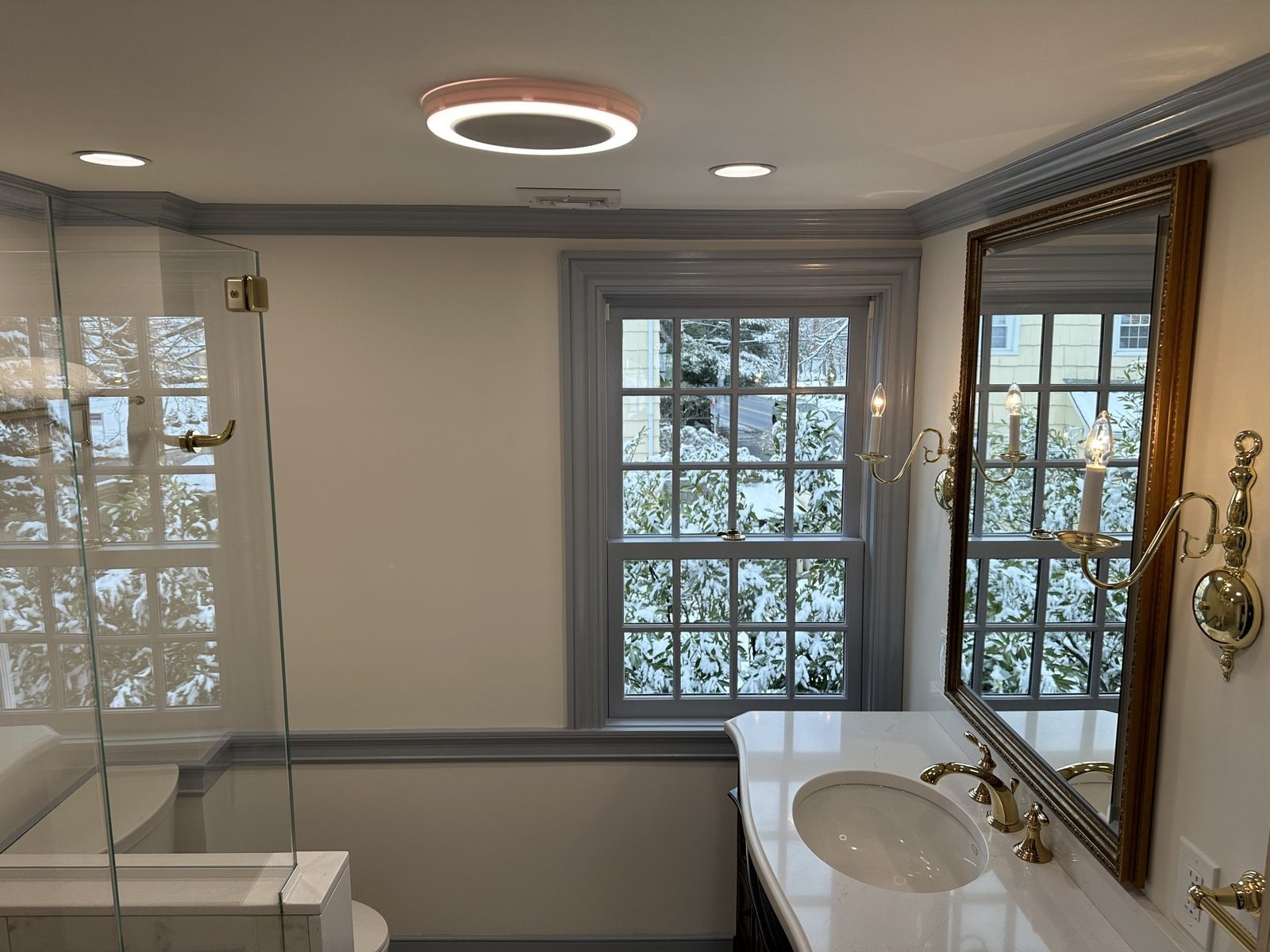 Transitional bathroom with porcelain tile flooring, glass-enclosed shower, framed medicine cabinet, and period sconces.